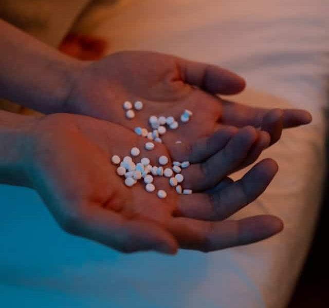 Hands holding white pills against a softly lit background in a bedroom setting