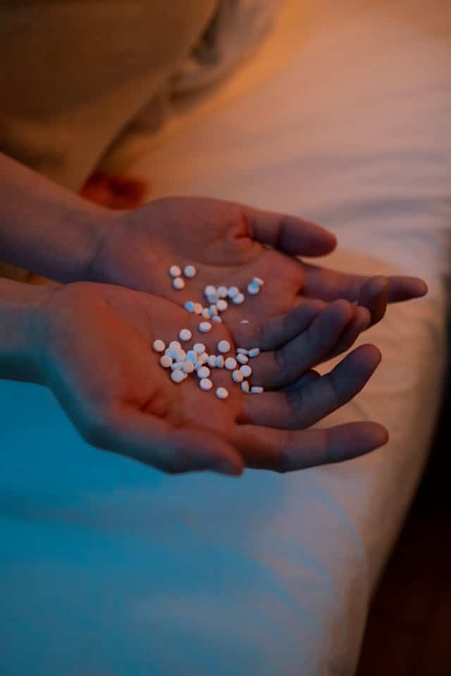 Hands holding white pills against a softly lit background in a bedroom setting